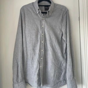 Grå skjorta från Oscar Jacobson - Klassisk grå skjorta från Oscar Jacobson i slim fit. Skjortan har knappar hela vägen, button down-krage och är långärmad. Tillverkad i mjuk bomull som känns skön mot huden. Perfekt till både jeans och chinos. Nästan aldrig använd