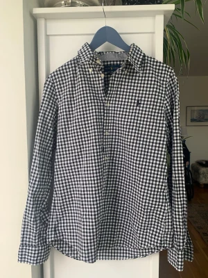 Rutig skjorta från Ralph Lauren - Klassisk svartvit rutig skjorta från Ralph Lauren i slim fit-modell. Skjortan har långa ärmar, knappar framtill och den ikoniska broderade loggan på bröstet. Tillverkad i mjuk bomull som känns skön mot huden. Perfekt för en clean och stilren look.