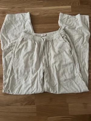 Beiga linnebyxor från Nelly - Säljer ett par beiga linnebyxor från Nelly i storlek XXS. Byxorna har resårmidja med dragsko och sidofickor. De är tillverkade i ett luftigt linnematerial och har en avslappnad passform som är perfekt för varma dagar. Uppsydda så passar folk som är från 150cm till 155cm lång.