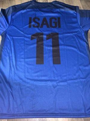 Blå Team Z Isagi tröja - Säljer en blå sporttröja med svarta detaljer från Team Z, inspirerad av karaktären Isagi med nummer 11 tryckt på både fram- och baksidan. Tröjan har rund hals och korta ärmar, perfekt för fotboll eller träning. Materialet är lätt och andas.