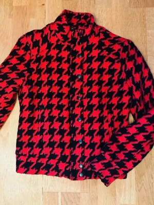 Vintage pepitarutig ulljacka röd/svart – retro 80–90-tal houndstooth vår & höst - Vintage pepitarutig jacka i rött och svart i ullblandning. Kort modell med dragkedja, tryckknappar och krage. Klassisk houndstooth/pepita som ger en snygg retrolook. Designen känns typisk för 80–90-talets stil.  Perfekt vår- och höstjacka som funkar lika bra till jeans, kjol eller helsvart outfit.  Storlek 36. Svart satinliknande foder.  Köpt second hand eftersom jag gillade mönstret, men den har mest blivit hängande i garderoben.  Mycket fint skick.  