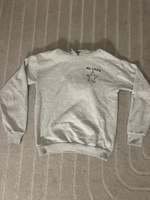 Grå sweatshirt med tryck Ma Chérie - Säljer en ljusgrå hoddie med svart tryck 'MA CHÉRIE' och en stjärna både fram och bak. Från Gina-Tricot. Storleken står ej men skulle tippa på 158-164/xs