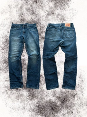 Levi’s 511 - Säljer ett par klassiska blå jeans från Levi's med rak passform och fem fickor. Jeansen har snygga slitningar och en vintage tvätt som ger en avslappnad look. Tillverkade i bomull med Levi's ikoniska läderpatch bak i midjan.