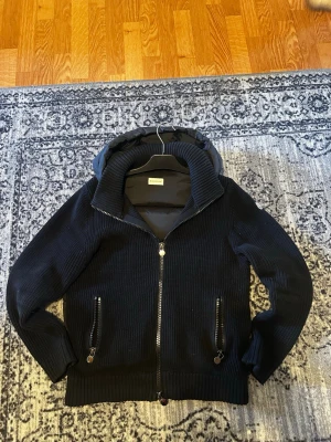 Moncler backpadded cardigan  - Säljer en svart backpadded cardigan från Moncler med stickade ärmar och quiltad kropp. Den har huva, två dragkedjeförsedda fickor fram och ribbade muddar. Perfekt för kalla vinterdagar och riktigt snygg streetstil som passar även nu till våren. Den här nfc-tag och man kan skanna, priset är ej hugget i sten så var inte rädda att ställa frågor 😁