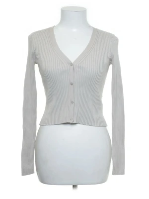 Beige ribbad kofta  - Snygg beige ribbstickad kofta med v-ringning och långa ärmar. Koftan har knäppning framtill med fyra knappar och är figurnära i modellen. Perfekt att styla över ett linne eller t-shirt för en trendig lager-på-lager-look.