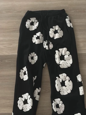 Svarta mjukisbyxor med vita blommor - Snygga svarta mjukisbyxor med stora vita blommönster över hela byxorna. Byxorna har resår i midjan och dragsko för skön passform. Perfekta för en avslappnad och trendig stil.