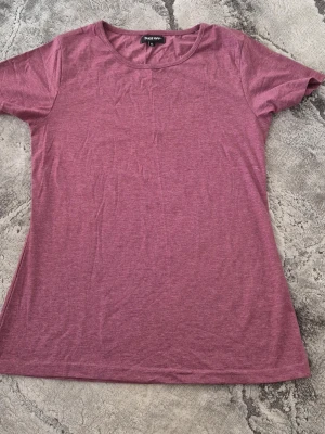 Mörkrosa t-shirt från Take Off - En enkel och stilren mörkrosa t-shirt från Take Off. T-shirten har rund halsringning och korta ärmar. Tillverkad i mjuk bomull som känns skön mot huden. Perfekt basplagg att matcha med jeans eller shorts.