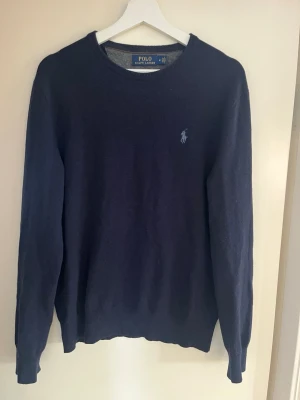 Mörkblå stickad tröja Ralph Lauren - Mörkblå stickad tröja från Ralph Lauren, ett litet hål som syns på tredje bilden, går att sy ihop enkelt men syns knappt vid användning 
