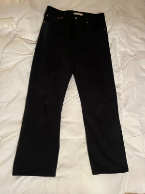 Svarta raka jeans från Levi's - Säljer ett par svarta jeans från Levi's med rak passform och klassisk femficksdesign. Jeansen har knappgylf och Levi's ikoniska läderpatch bak i midjan. Perfekta för en clean och stilren look.