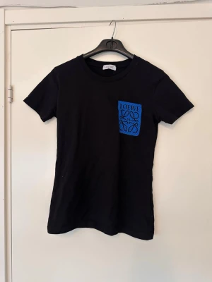 Svart  t-shirt med blå ficka - Snygg svart t-shirt med blå bröstficka som har, T-shirten har rund hals och korta ärmar, perfekt för en clean och stilren look. Tillverkad i mjuk bomull för maximal komfort.
