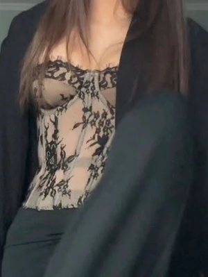 Beige spetskorsett med svart brodyr - Trendig beige korsett med svart spetsbrodyr och markerade kupor. Snygg genomskinlig mesh och figurnära passform. Perfekt att styla med kavaj eller kjol för en cool look.