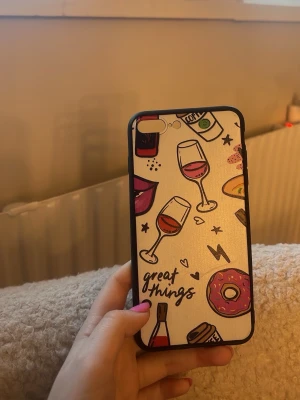Färgglatt mobilskal med motiv - Mobilskal med vit bakgrund och färgglada illustrationer av vinglas, donut, läppar och texten 'great things'. Skalets kanter är svarta och det är gjort i plast. Passar till iPhone med dubbla kameror.