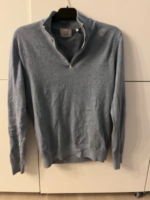 Blå halvzip tröja från Bläck - Snygg blå långärmad tröja från Bläck med halv dragkedja och ståkrage. Tillverkad i mjukt material, perfekt för lager på lager. Ribbstickade muddar vid ärmslut och nederkant ger en clean look. Tröjan är endast använd 2-3 ggr och är i storlek S