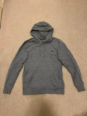 Grå hoodie från J.Lindeberg - Mysig grå hoodie från J.Lindeberg med klassisk huva och dragsnören. Tillverkad i mjukt bomullsmaterial. Perfekt för chill dagar eller när du vill ha en clean look. Hör av dig vid prisförslag eller andra funderingar!😊