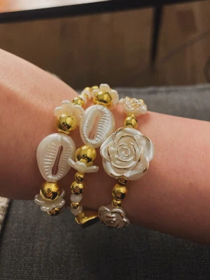 Guldiga armband med pärlor - Säljer 3 handgjorda armband! 2 av dem har en magnetisk hjärtberlock och 1 extra med vita och guldfärgade blommor 🥰