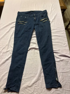 Mörkblå skinny jeans med dragkedjor - Säljer ett par mörkblå skinny jeans med flera coola dragkedjor framtill och vid bensluten. Jeansen har låg midja, smal passform och bakfickor. Materialet känns stretchigt och bekvämt, perfekta för en trendig look.