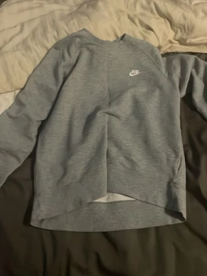 Grå sweatshirt från Nike - Säljer en stilren grå sweatshirt från Nike med klassisk logga broderad i vitt på bröstet. Tröjan har rund halsringning och långa ärmar. Perfekt för en avslappnad och sportig look.