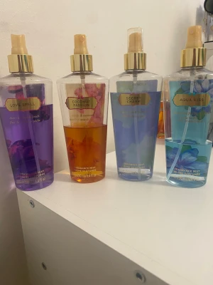 Victoria's Secret Body Mists 4-pack - Fyra olika body mists från Victoria's Secret: Love Spell (lila), Coconut Passion (gul/orange), Secret Charm (ljusblå) och Aqua Kiss (blå). Flaskorna är genomskinliga med guldfärgade spraymunstycken och etiketter. Varje flaska rymmer 250 ml och har blommiga och fruktiga doftnoter.