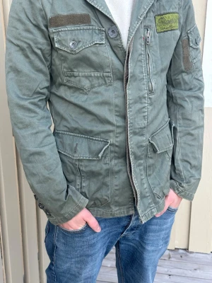 Grön fieldjacket från Jack and jones - Schysst vintage field jacket från jack and jones i olivgrönt. Killen på bilden är 180, skriv vid minsta fråga. Perfekt inför våren