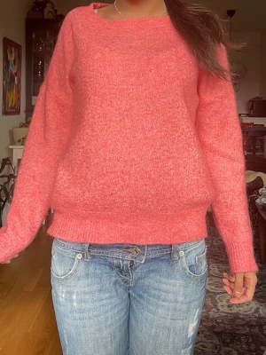Korall stickad tröja med rund hals - Mysig korall stickad tröja med rund halsringning och långa ärmar. Tröjan har en avslappnad passform och ribbstickade muddar vid ärmslut och nederkant. Perfekt för att hålla värmen under kyliga dagar.