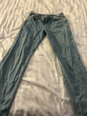 Ljusblå low/midwaist raka jeans från NA-KD - Säljer ett par ljusblå jeans från NA-KD med rak passform och klassisk femficksdesign. Jeansen har låg-mid midja och är tillverkade i denim med dragkedja och knapp framtill.