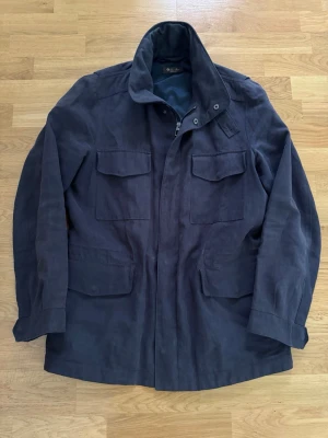 Loro Piana Traveler Cotton and Linen-blend rain system - Säljer nu denna extremt trevliga fieldjacket, Loro pianas Traveler är en tidlös jacka som passar till alla tillfällen, denna är sval och passar perfekt till en regnig sommar dag, sommar kväll eller en perfekt jacka att kasta över sig vid en middag. Storlek 48/S-M. Ny pris 30 000kr säljer för ett riktigt fint pris.