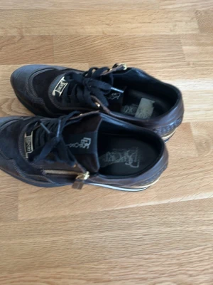 Svarta sneakers från Iceberg - Snygga svarta sneakers från Iceberg med gulddetaljer och dragkedja på sidan. Skorna har en mix av mocka och läder, samt snörning framtill. Perfekta för dig som vill ha en unik och trendig look.
