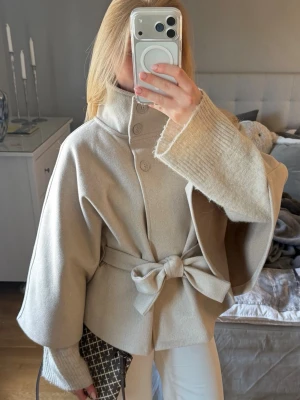 Beige cape kappa - storlek XS/S - Säljer en helt ny Cape kappa från Gina tricot i storlek XS/S. Den har ett bälte i midjan och två knappar för en högre krage, man kan också börja kappan öppen. Så himla fin färg och passar till allt. Aldrig använd så helt ny och i perfekt skick. Hör gärna av dig vid frågor💗