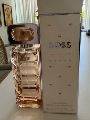 BOSS Woman Eau de Toilette 30ml - BOSS Woman Eau de Toilette i elegant vit och guld kartong. Flaskan innehåller 30 ml och har en stilren design med silverfärgade detaljer. En klassisk parfym som utstrålar modern och feminin känsla.