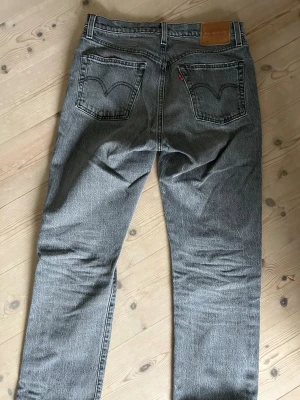 Grå Levi's 501 jeans - Säljer ett par grå Levi's 501 jeans med klassisk rak passform och knappgylf. Jeansen har fem fickor, tydliga sömmar och den ikoniska läderpatchen bak i midjan. Materialet är kraftig denim i bomull med en snygg tvättad look.
