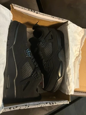 Svarta Air Jordan 4 Retro sneakers - Snygga helsvarta Air Jordan 4 Retro sneakers med ikonisk Jumpman-logga på plösen. Skorna har meshpaneler, läderdetaljer och plastvingar på sidorna. Klassisk siluett med tjock sula och coola detaljer som gör dem till ett måste för alla sneakerheads.