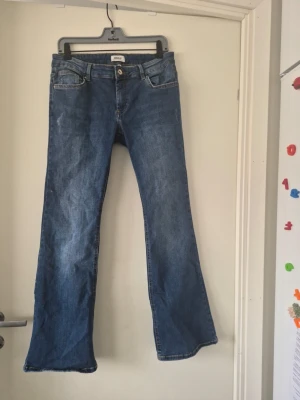 Blå bootcut jeans från ONLY - Säljer ett par klassiska blå bootcut jeans från ONLY. Jeansen har fem fickor, bälteshällor och stängs med knapp och dragkedja. Materialet är denim i bomull och passformen är utsvängd nedtill för en snygg retrostil.