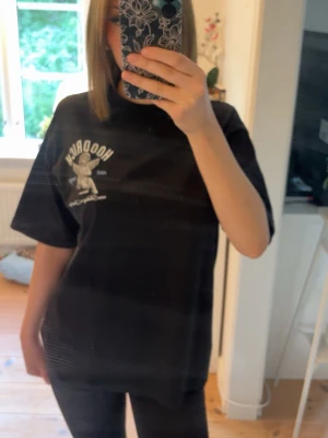 Svart t-shirt med ängeltryck HOODRICH - Svart t-shirt från Hoodrich med tryck av en ängel och text på bröstet, även på ryggen.  Oversized passform och rund halsringning. Perfekt för en avslappnad streetwear-look. Storlek XS passar som S eller M