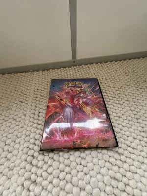 Pokémon samlarkortpärm med kort Alla är ej originalla - Säljer en färgglad Pokémon samlarkortpärm med motiv av Urshifu på framsidan. Pärmen innehåller flera Pokémonkort i plastfickor, både vanliga och holografiska. Perfekt för dig som vill utöka din samling eller börja samla Pokémonkort.
