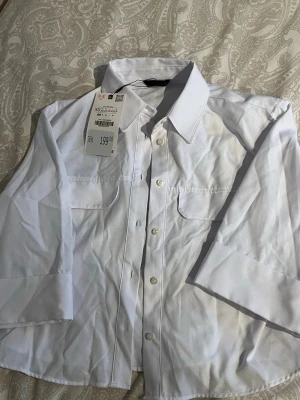 Vit crop top skjorta från ZARA🤍 - Klassisk vit crop top skjorta från ZARA som alla behöver!🫶🏼 Snygg och väldigt enkel att styla med allt! Har två bröstfickor och knappar, beroende på hur man vill ha den! Helt ny och kommer även med prislappen, aldrig använt❤️❤️Orignalt priset är 199kr!