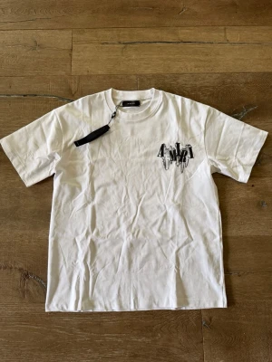 Vit AMIRI t-shirt med tryck - Snygg vit t-shirt från AMIRI med svart tryck på bröstet och stor logga med kedjedetaljer på ryggen. Klassisk passform och rund hals.
