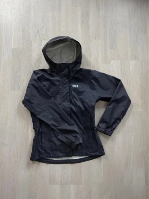 Svart regnjacka från Helly Hansen - Jättefin marinblå vindjacka från Helly Hansen i storlek XS som tyvärr inte kommit till användning. Superfint skick, en ett litet hål på vänster arm som inte syns när man har jackan på sig (se andra bilden) 💙