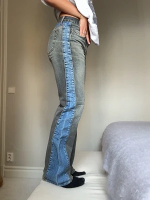 Grå jeans med blå sidopanel - Unika grå jeans med breda blå sidopaneler och raka ben. Jeansen har hög midja, klassiska fem fickor och kontrastsömmar. Perfekta för dig som vill sticka ut med en cool och trendig look.