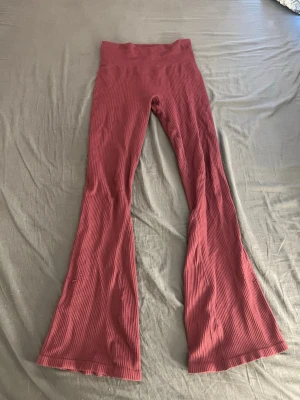 Vinröda ribbade flare leggings 157 - Säljer ett par vinröda leggings från 157 med ribbad struktur och utsvängda ben. Modellen heter Flare och har hög midja för en snygg siluett. Materialet är stretchigt och mjukt, perfekt för dig som gillar bekväma men trendiga byxor. Se dom 2 sista bilderna, byxorna är lite slitna nere vid bena