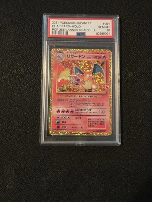 Charizard Holo Pokémonkort 25th Anniversary - Japanskt Charizard Holo Pokémonkort från 2021, 25th Anniversary Edition. Kortet är graderat av PSA och har en glittrig holografisk yta med röd och gul design. Kortet ligger i ett genomskinligt plastskydd med etikett.pris kan diskuteras 