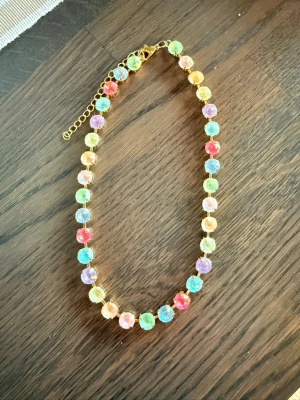 Färgglatt halsband med pärlor - Säljer ett halsband med stora, multifärgade stenar i regnbågens färger. Stenarna är 8 mm stora och sitter i guldfärgade fästen med justerbart lås. Perfekt för dig som vill ha en färgklick till din outfit!