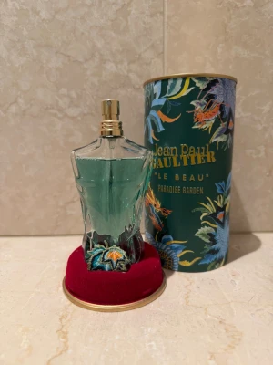 Jean Paul Gaultier Le Beau Paradise Garden - Parfymflaska i form av en manlig torso med turkosgrönt innehåll och guldfärgad spraykork. Flaskan har broderade detaljer med tropiska motiv och kommer med en dekorativ grön tub med färgglada blommor och djur. Volymen är 75 ml. Bara användbar 3 ggr ungefär så ganska prisvärd! Pris kan diskuteras 