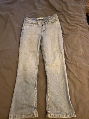Ljusblå bootcut jeans - Säljer ett par ljusblå bootcut jeans med klassisk femficksdesign och snygga kontrastsömmar på bakfickan. Jeansen har normal midja och är tillverkade i mjukt denimtyg som ger en avslappnad look. Perfekta för dig som gillar retrostil och vill ha ett par bekväma jeans. Jeans från Lindex. Storleken är märkt 19 enligt etiketten, men upplevs mer som en  s