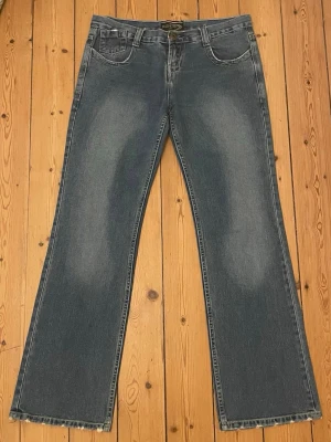 Blå lowrised bootcut jeans med slitna detaljer samt gul sömning - Ett par blå super lowrised bootcut jeans med ljusa slitningar framtill och bak, fransiga benslut. Klassisk femficksmodell med bälteshällor och dragkedjegylf. Jeansen har en avslappnande men super snygg 2000s look som passar i alla tillfällen 🩵🩵🩵 storleken är 46 men passar mig som använder storlek 38/40 i vanliga fall