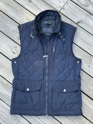 Mörkblå quiltad dunväst Zara Man - Snygg mörkblå quiltad dunväst från Zara Man med hög krage och spänne, dragkedja framtill, bröstficka med dragkedja och två stora fickor med lock. Perfekt för lager på lager och stilren look. Materialet är lätt och vadderat, perfekt till sommar och höst ⛱️ Tveka inte att höra av dig vid minsta fråga eller fundering 🙏🙌