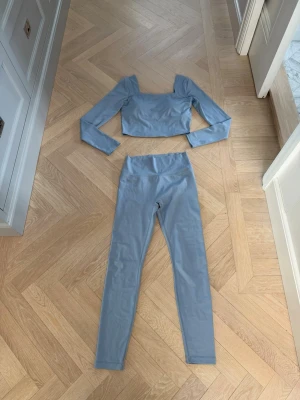 Sisterly Tribe- Ljusblått set med långärmad topp - Snyggt ljusblått set från Sisterly Tribe med långärmad, croppad topp och matchande höga tights. Setet har en modern, minimalistisk look med fyrkantig ringning och stretchigt material som tightar till. Perfekt för dig som gillar stilrena och snygga träningsplagg. Toppen är i Size M och tightsen i L