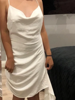 Vit klänning  - Säljer en vit kortklänning med tunna axelband och omlottdetalj. Klänningen har en draperad urringning och lätt asymmetrisk nederkant. Materialet känns lätt och svalt, perfekt för varma dagar. Köpte denna i Los angeles för ungefär 800kr