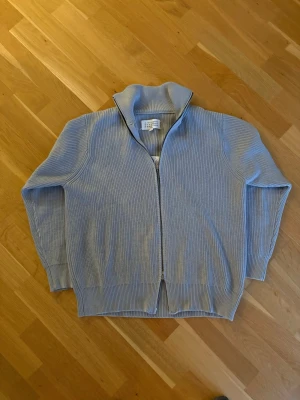 Ljusgrå stickad ziptröja från maison margiela - Ljusgrå stickad tröja från Maison Margiela med dragkedja framtill och hög krage. Perfekt för lager på lager och enkel att matcha till olika outfits. Storleken är 46 och passar som M/L