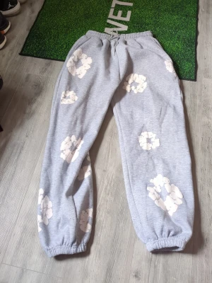 Grå mjukisbyxor med vita tryck - En blomma har spräckt lite men inget man tänker på Säljer ett par grå mjukisbyxor med vita, molnliknande tryck över hela byxorna. Byxorna har resår i midjan och vid bensluten för en skön och avslappnad passform. Perfekta för chill dagar hemma eller när du vill ha en casual look.