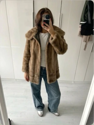 Beige pälsjacka med bred krage - Snygg beige pälsjacka med bred krage och rak passform. Jackan har en mjuk, lyxig känsla och är fodrad med rosa tyg på insidan. Perfekt för att hålla värmen under kalla dagar. 